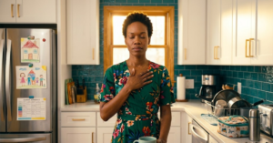 Why You Can Have Peace Without Having It Together Black woman in deep green floral wrap dress, eyes closed hand on chest in kitchen amid the mess, teal backsplash, gold window light